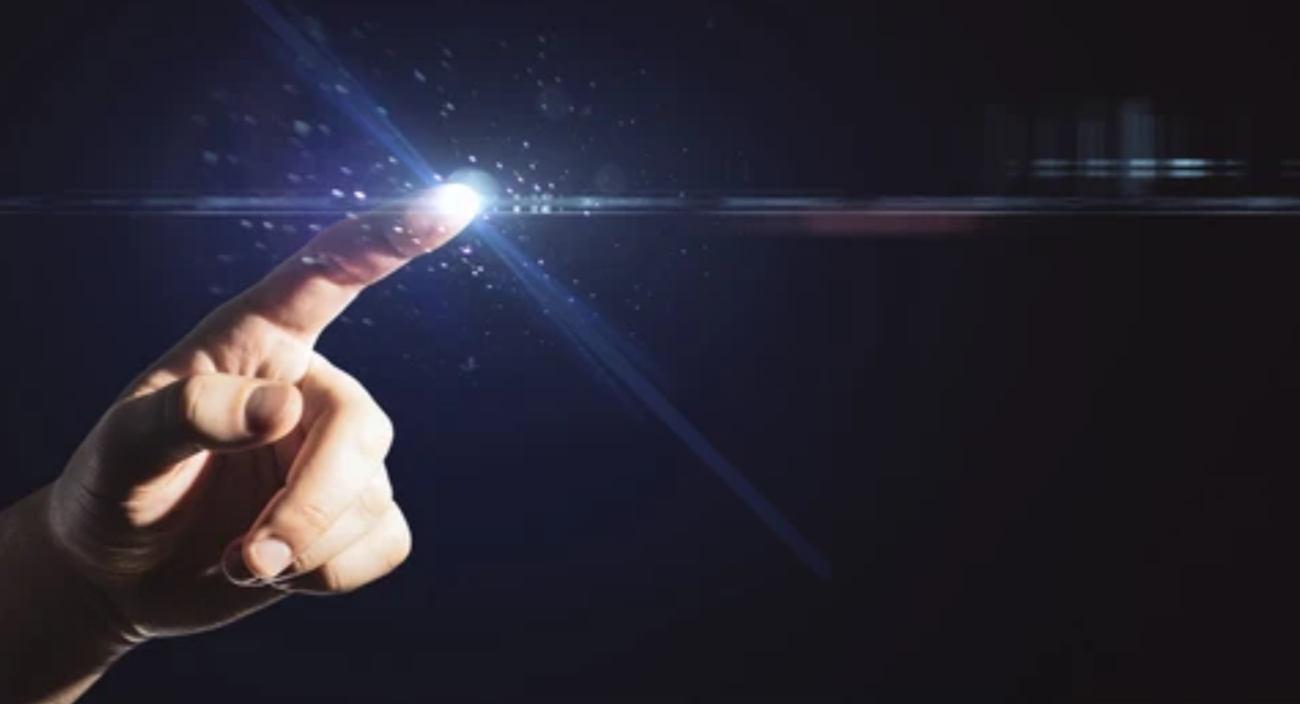 A fingertip touching a point of light on a dark screen, sparks scattering from it.